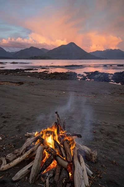 A vertical shot of a campfire on lake shore during sunset
