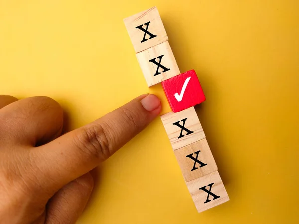 黄色の背景にチェックマークの付いた赤い木製のブロックを押す指 — ストック写真
