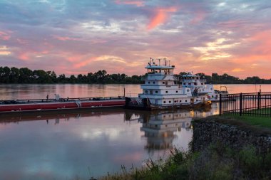 A large cruise ship moored on the Ohio River pier under a pink sunset sky