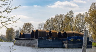 A closeup of barges with monopiles in an industrial harbor in Roermond