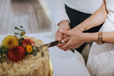 A closeup of the bride and groom cutting a cake decorated with flowers at a wedding