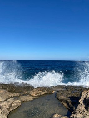 A vertical shot of blue seascape crashing against rocky beach on a sunny day in Cyprus