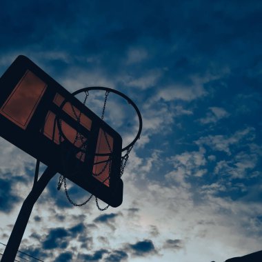 A low angle shot of a basketball hoop against a cloudy sky