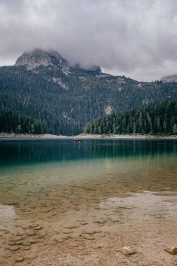 Göl ve yeşil bitki örtüsüyle kaplı dağın dikey görüntüsü. Karadağ 'da yürüyüş.