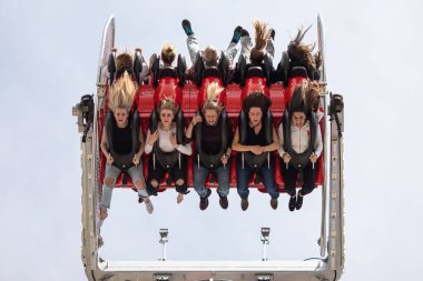 A low angle shot of people sitting on a carousel and shouting with adrenaline as the wind blows