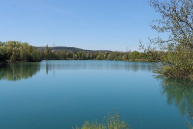 Almanya 'nın Bavyera şehrinde güneşli bir günde yeşil ağaçlarla çevrili bir gölün manzarası