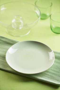 A vertical closeup shot of an empty plate, glasses served on a pastel green tablecloth