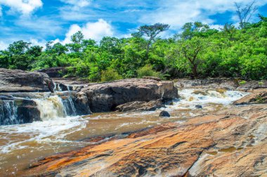 Bulutlu mavi gökyüzü. Çiftlikteki orman. Kayalara düşen şelale..