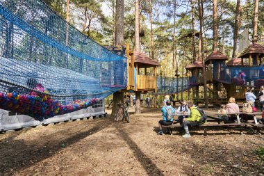 A Group of parents sitting on a wooden table and bench watching their kids at the Pyrland climbing park in Poznan, Poland