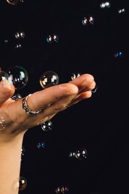 woman holding up flattened hand gesturing to floating, touchable bubbles on black background