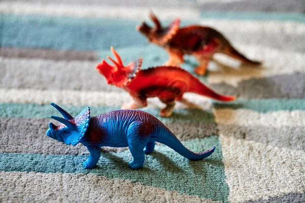 A closeup shot of a triceratops dinosaur toy on the carpet in bright light with other dinosaur toys in the blurred background