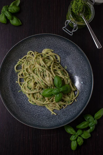 A vertical closeup of traditional Italian pasta with pesto sauce and basil leaves served on a ceramic plate