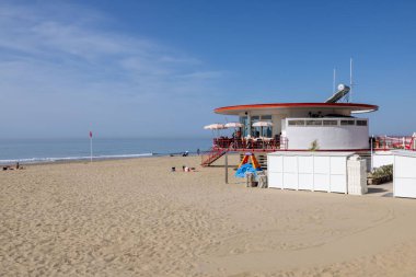 A sunny sandy beach with a small round cafe under the clear blue sky
