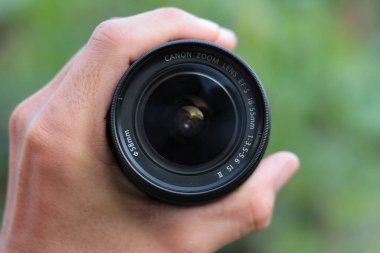 A black canon kit lens in a man's hand on a blurry background