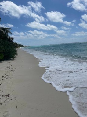 A vertical shot of blue ocean waves hitting the beach in cloudy sky background