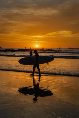 Kosta Rika 'da okyanus kıyısında sörf tahtası tutan bir adamın dikey çekimi.