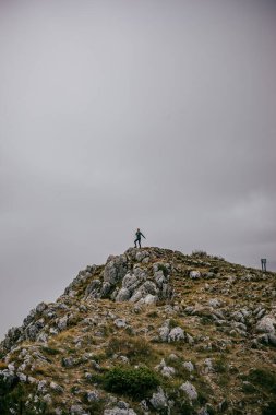 A vertical shot of the person standing on the mountain peak against cloudy sky. Hiking, Montenegro.