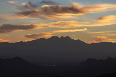 Canlı bir günbatımı arka planında bir dizi kayalık dağın silueti.