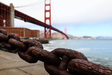 A blurred view of the Golden Gate Bridge behind rusted metal chains in San Francisco, California