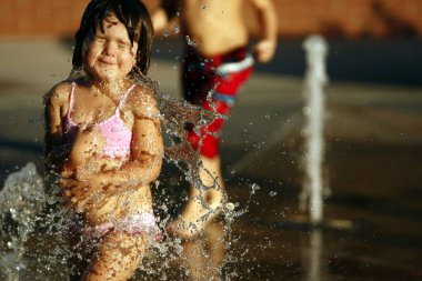 A young girl enjoying the water fountain in the middle of summer late in the afternoon