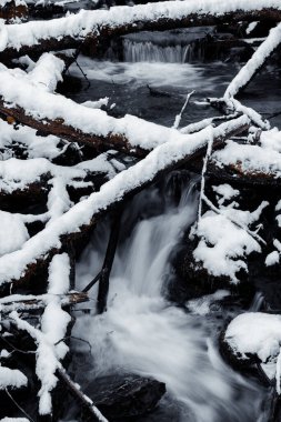 Kışın karla kaplı kayalardan akan bir şelalenin dikey görüntüsü.