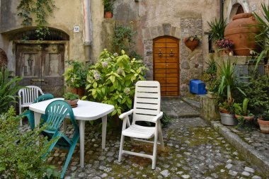 Sokaktaki masanın etrafındaki boş sandalyeler yeşil bitki örtüsüyle çevrili. Lenola, Lazio, İtalya.
