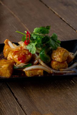 A plate of Dragon paneer served with chopped fresh greens on a wooden table