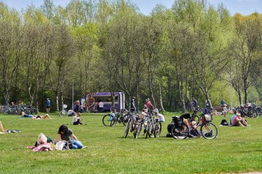 The people resting on green grass by the Rusalka lake on a sunny spring day