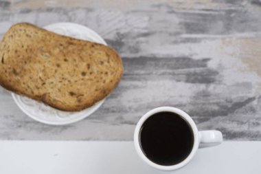 A top view of a cup of coffee with sliced bread  on a gray table