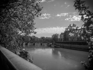 A grayscale shot from a bridge of a river with buildings on the other side and trees