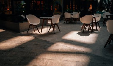 A scenic view of modern tables and white chairs in sunlight in a cafe