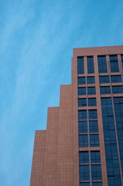 A low angle shot of a modern style building with glasses from top to bottom under a clear sky