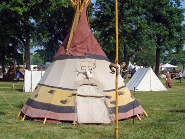 An Indian style tent on a meadow surrounded by trees in a daylight