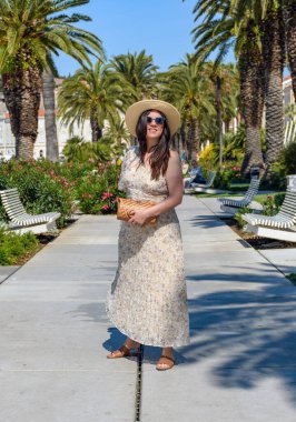 A vertical shot of a Caucasian woman in sunglasses in a summer dress on a promenade in Split, Croatia