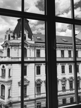 A grayscale shot of a buildng with gray cloudy sky behind a glass window in Prague, Czech Republic