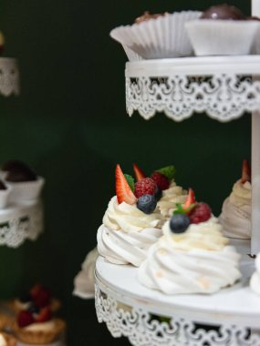 A vertical shot of meringues with raspberry, strawberry, and blueberry on a tray