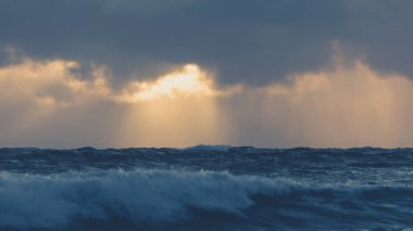 Güneşin güzel bir görüntüsü bir deniz manzarasının üzerindeki bulutların arkasında saklanıyor.