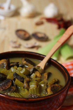 A vertical shot of a delicious bowl of green mushroom and celery   broth with a spoon