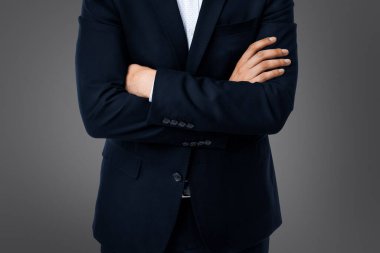 A businessman with crossed arms on grey background standing firmly in front of the camera