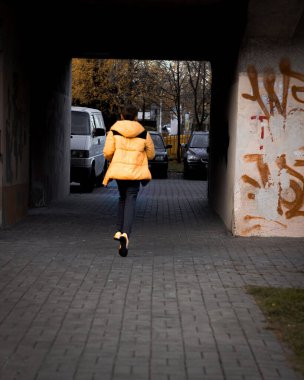A vertical back view of a kid running on a cobblestone alley between buildings