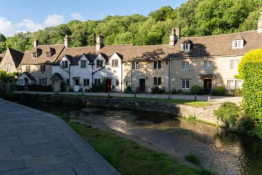 The brown stone cottages surrounded by green vegetation. Castle Combe, England, UK.
