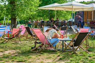 Güneşli bir günde parkta sandalyede oturan insanların görüntüsü.