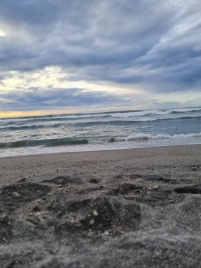 Bulutlu bir günde kumlu bir sahilde köpüklü yumuşak okyanus dalgaları