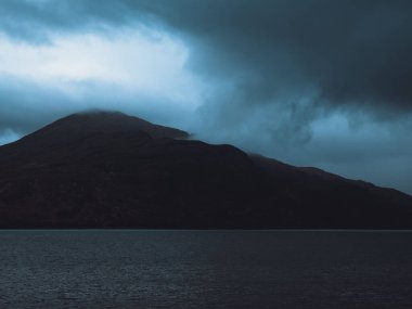 A beautiful view of a lake surrounded by mountains under dark storm clouds