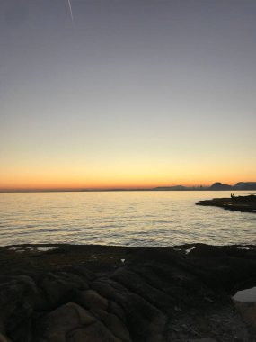 Dalgalı bir denizin dikey görüntüsü gün batımında renklenen dağların arka planında.