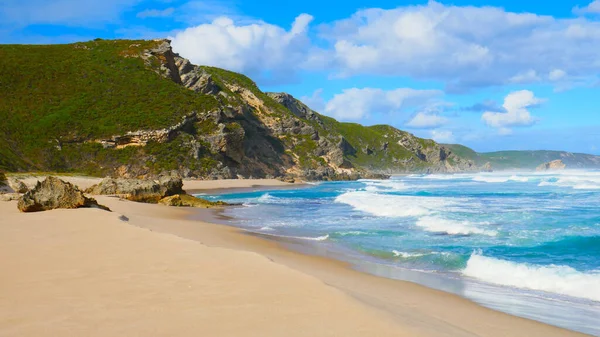 Beautiful sandy beach hugging a massive cliff and lovely ocean,