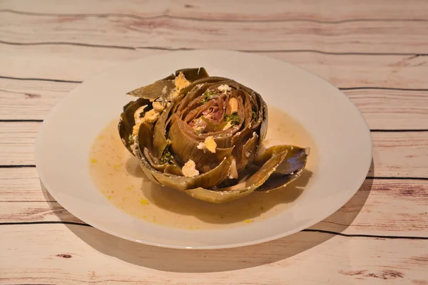 boiled artichoke on white plate on wooden table italian style stuffed with egg, parsley, garlic , typical mediterranean food