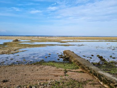 A small and old damaged pier made with stones on a big pond under cloudy sky
