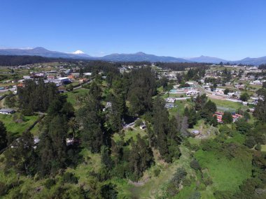 Güneşli bir günde yeşil ormanlarla kaplı tepelerin ve kırsal alandaki evlerin kuş bakışı görüntüsü