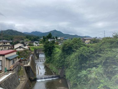 A river flowing between houses and trees with mountains in the background
